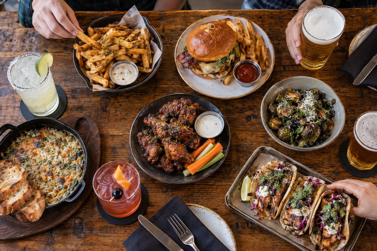 Overhead view of custom tavern dishes and drink pairings on a wooden table